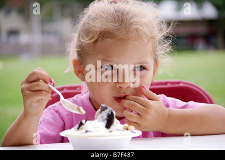 Une fillette de quatre ans biracial mange un bol de crème glacée à un pique-nique. Banque D'Images