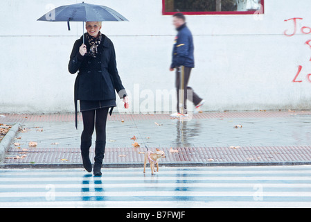 Jeune femme blonde marcher avec son animal de compagnie sous la pluie Banque D'Images