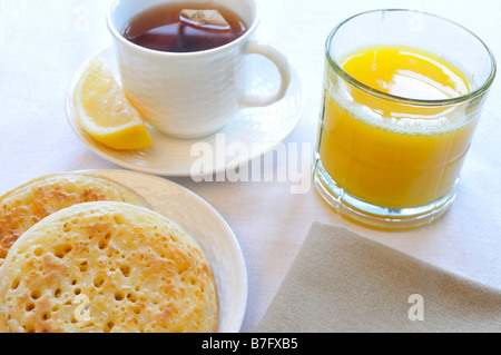 Crumpets sur plaque blanche avec verre de jus d'orange, une tasse de thé noir avec du citron et serviette sur fond blanc. Banque D'Images