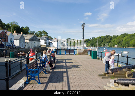 Un petit enfant grimpe sur un canon sur Fowey Quayside aidé par sa mère d'autres visiteurs s'asseoir sur des bancs Banque D'Images