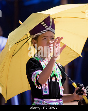 Une jeune fille Hmong en costume traditionnel se prépare à attraper une balle lors d'une cérémonie du Nouvel An Hmong, à l'ombre d'un parasol jaune. Banque D'Images
