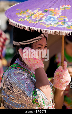 Une femme Hmong en costume traditionnel combiné avec des mitaines rose est à l'ombre d'un parasol violet comme elle parle sur son téléphone mobile. Banque D'Images