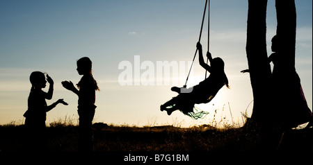 Silhouette de filles indiennes se balançant et mains dans la campagne de l'Inde rurale au coucher du soleil. L'Andhra Pradesh, Inde. Vue panoramique Banque D'Images