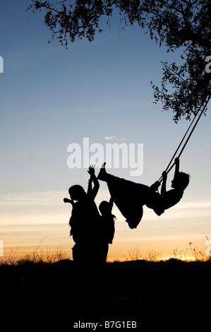 Silhouette de filles indiennes se balancer sur une balançoire faite maison dans la campagne de l'Inde rurale au coucher du soleil. L'Andhra Pradesh, Inde Banque D'Images