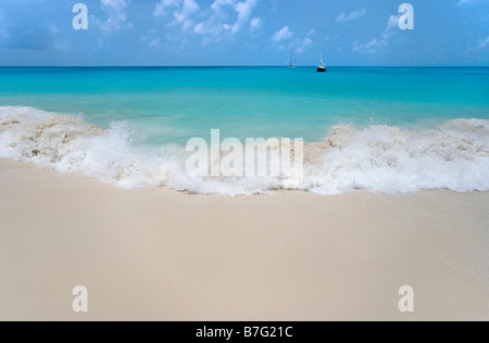 Une vague se brise sur 11 Mile Beach-Barbuda Antilles comme deux voiliers de croisière reste à l'ancre au large des côtes Banque D'Images