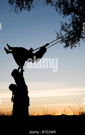 Silhouette de filles indiennes se balancer sur une balançoire faite maison dans la campagne de l'Inde rurale au coucher du soleil. L'Andhra Pradesh, Inde Banque D'Images