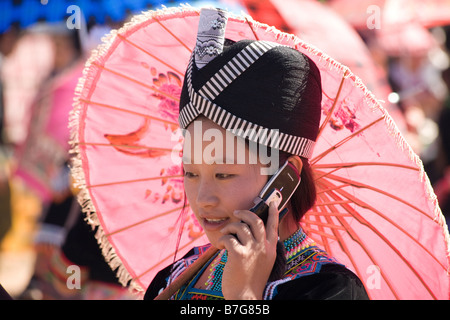 Une fille Hmong vêtements traditionnels parle sur son téléphone mobile, à l'ombre de son parasol rose, lors d'une célébration du Nouvel An Hmong. Banque D'Images