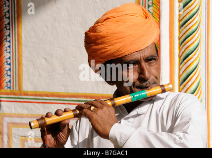 Un homme avec une moustache et un turban orange joue une flûte de bambou Banque D'Images