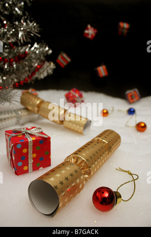 C'est un studio shot of Christmas crackers et babioles contre un arbre avec parcelles tombant contre un ciel noir Banque D'Images