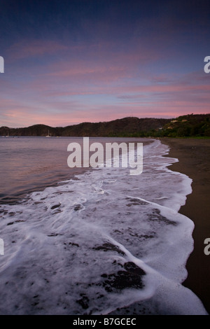 Vagues sur la côte volcanique lave de Playas del Coco, Costa Rica au crépuscule. Banque D'Images