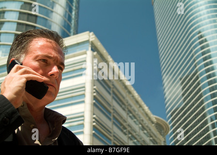 Un homme sur un téléphone cellulaire avec de grands immeubles de bureaux de verre se dessinent dans l'arrière-plan Banque D'Images