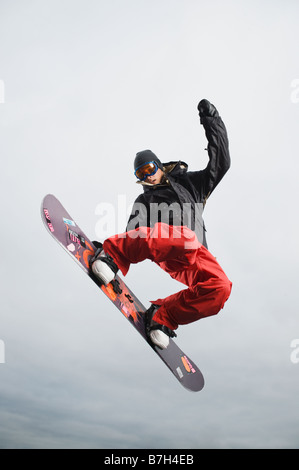 Mixed Race teenager à la mi-air au snowboard Banque D'Images