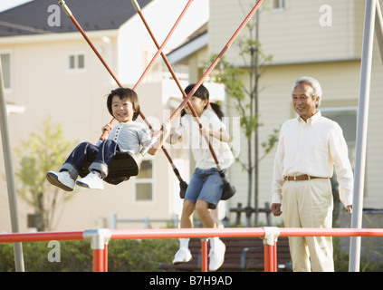 Grand-père et ses petits-enfants jouant sur la balançoire Banque D'Images