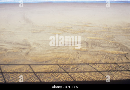 Plage de sable déserte propre criblée avec marée séchées ondulations avec la mer au loin sur un bord et l'ombre des garde-fous aux autres Banque D'Images