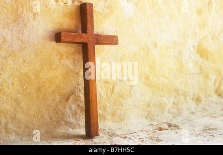 Petit crucifix en bois debout dans une lumière chaude contre mur peint crème dans fenêtre Banque D'Images