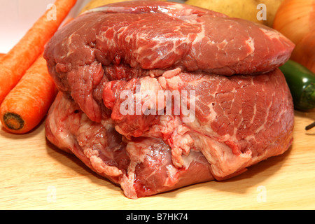 Rôti de bœuf cru sur une planche à découper avec légumes en arrière-plan Banque D'Images