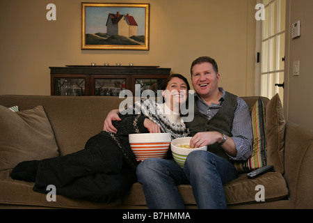 Un couple et de grignoter tout en regardant la TV sur leur canapé. Banque D'Images