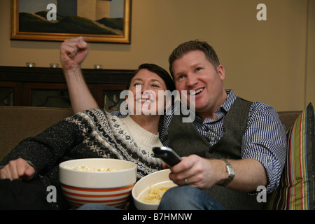 Un couple et de grignoter tout en regardant la TV sur leur canapé. Banque D'Images