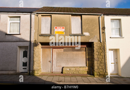 Fenêtres et portes placardées sur maison mitoyenne en pierre partiellement plaqués d'agents immobiliers vendus en regard de l'établissement bien entretenu UK Banque D'Images