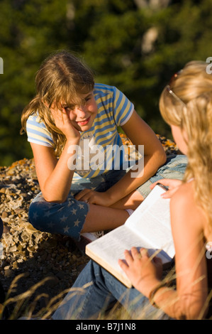 Deux soeurs assis en plein air, la lecture d'un livre, en Saskatchewan Banque D'Images