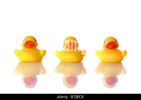 Trois petits canards en caoutchouc assis dans une rangée avec la réflexion sur la surface blanche Banque D'Images
