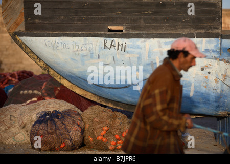 Un pêcheur passe devant un bateau de pêche traditionnel au port d'essaouira maroc Banque D'Images