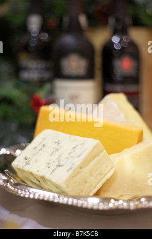 Briques de bleu, cheddar, parmesan et fromage brie dans un plat en argent avec bouteilles de porto en arrière-plan Banque D'Images