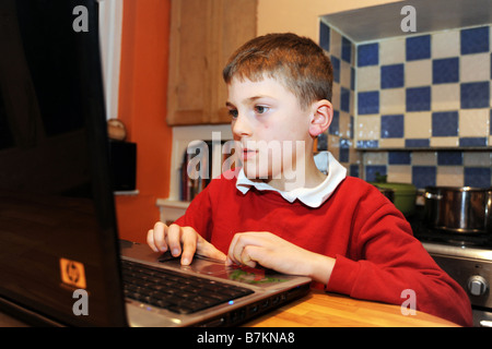 Un garçon de huit ans utilise l'ordinateur portable pour faire ses devoirs dans la cuisine Banque D'Images