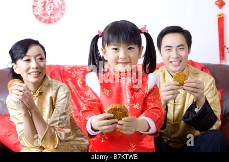 Jeune famille avec un enfant tenant des gâteaux de lune et souriant joyeusement Banque D'Images