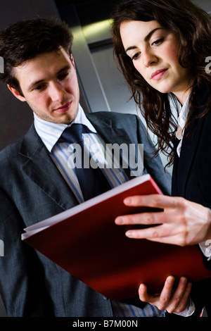 Les jeunes gens qui travaillent ensemble à l'office corridor à rouge à la lecture de rapports dossier document Banque D'Images