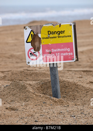 Le Signe de danger partiellement enterrée SOUS LE SABLE SUR LA PLAGE À ECCLES ON SEA EAST ANGLIA NORFOLK ENGLAND UK Banque D'Images