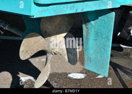 Usé et dénoyautés avec gouvernail et hélice bronze fond vert peinture sur le fond d'un bateau en fibre de verre. Banque D'Images