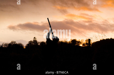 Hunter avec fusil en silhouette au coucher du soleil Banque D'Images