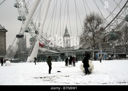 Les enfants jouent dans la neige en face de l'oeil de Londres tout en faisant un bonhomme de neige Banque D'Images