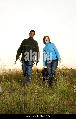 Couple walking dog outdoors au coucher du soleil en Californie sur hill Banque D'Images