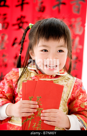 Fille en vêtements traditionnels chinois détenant des enveloppes rouges et rire permanent Banque D'Images