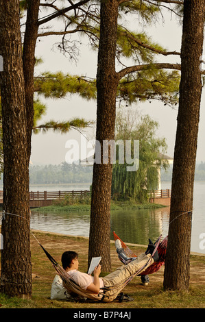 Man reading book in hammock, Lac Xuanwu Nanjing Chine Banque D'Images