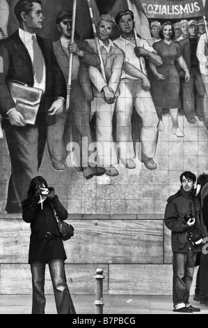 Deux touristes en face d'une peinture murale pour la gloire du socialisme, sur le bâtiment du Ministère de l'air du Reich, l'Allemagne. Banque D'Images