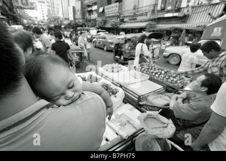 Petit bébé dormir sur l'épaule le long de la route à côté de parents fort trafic sur Thanon Yaowarat dans Chinatown Bangkok Thaïlande