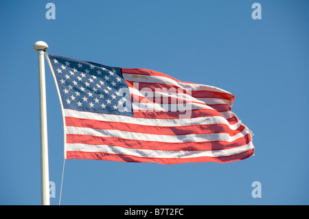 Drapeau américain fané volant sur un mât blanc vu contre un ciel bleu. Banque D'Images
