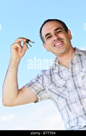 Smiling man holding clés de maison sur fond de ciel bleu Banque D'Images