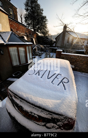 Voiture garée sur une allée AVEC DES MOTS SKIVER ÉCRIT DANS LA NEIGE qui suggère l'ABSENTÉISME AU TRAVAIL PENDANT LES CONDITIONS HIVERNALES MODÉRÉES U Banque D'Images