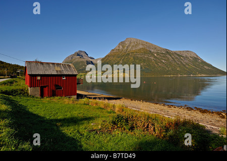 Hangar à bois rouge Lia avec l'île de Aldra et le Hjarttinden peaks derrière le nord-ouest de la Norvège Banque D'Images