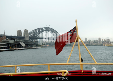 Red Ensign flying over top-deck coin et garde-corps de ferry du Port de Sydney, Sydney Harbour Bridge, avec en arrière-plan. Banque D'Images