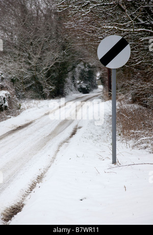 La limite de vitesse nationale britannique (60 mph ou 70 mph) sur une route couverte de neige avec les arbres. Banque D'Images
