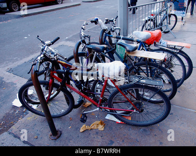 Streetworn et bien utilisé des Bicyclettes avec sièges recouverts de sac enchaîné à un porte vélo près d'une rue animée de la ville de New York. Banque D'Images