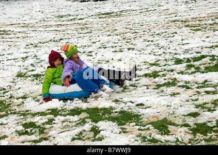 Deux jeunes filles s'amusant faisant glisser en bas de la colline dans la neige UK Banque D'Images