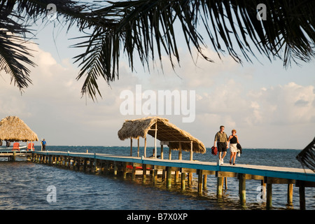 Couple d'Ambergris Caye BELIZE descendre pier vers restaurant des toits de chaume sur les structures du quai des eaux des Caraïbes palmier Banque D'Images