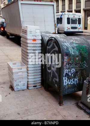 Des bacs en plastique ondulé empilé à côté de deux boîtes de stockage mail couvert de graffitis sur le trottoir à New York City. Banque D'Images