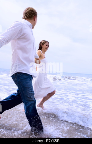 Un couple romantique tient les mains et éclabousse dans l'eau de l'océan à la plage. Banque D'Images